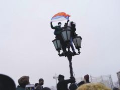 Два человека на фонаре во время митинга. Один с плакатом 